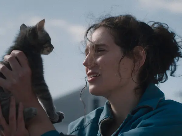 Woman smiling and cuddling black cat against cloudy sky.