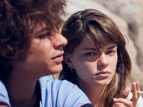Two people, a young man and woman, with serious expressions, looking intently at each other.