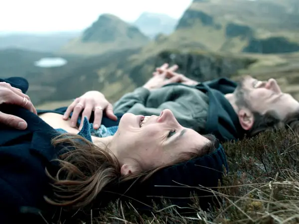 Two people lying on grass against mountainous backdrop.