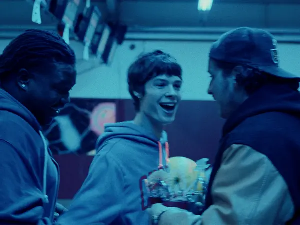 Three young men in casual clothing, one smiling broadly, engaged in lively conversation.