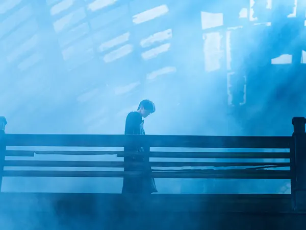 Silhouette of a person seated on a bench in a misty, blue-toned environment.