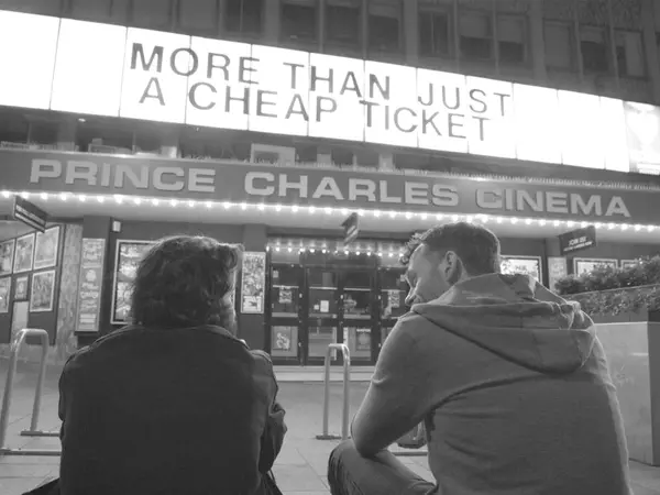 Black and white image showing two people from behind facing Prince Charles Cinema entrance with "More than just a cheap ticket" signage above.
