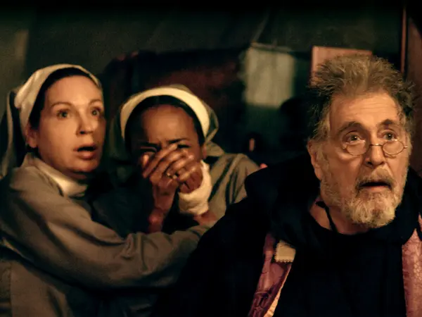 Three people, a woman in a headscarf covering her mouth, a woman with a concerned expression, and an older man with a beard, sitting together in a dimly lit room.