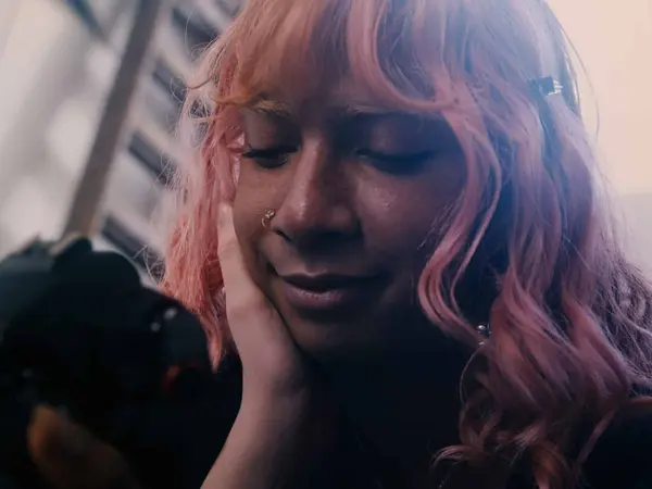 A woman with long, pink hair and eyes closed, appearing pensive or thoughtful.