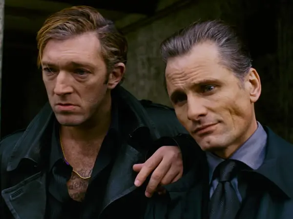 Two men wearing dark jackets and ties in a sombre expression.
