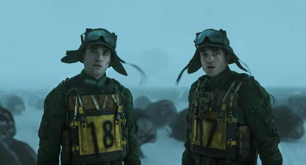 Two young soldiers in military uniform and helmets standing in a snowy, foggy landscape.