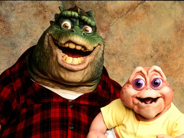 Two anthropomorphised green and pink monster characters with exaggerated features and expressions, wearing checked and yellow shirts against a textured brown background.